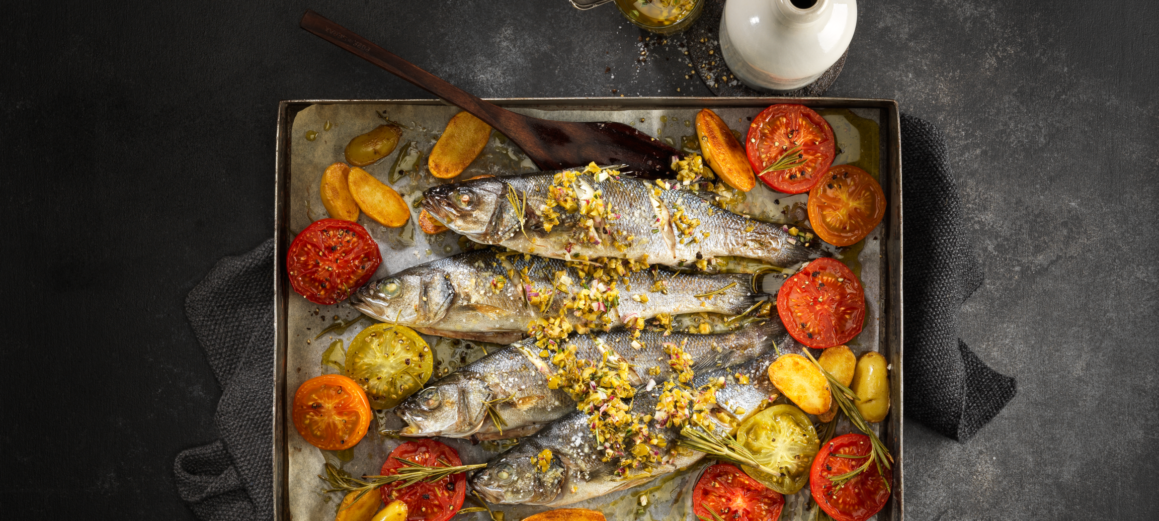 Bar cuit au four avec des petites pommes de terre, des tomates et du romarin, accompagné d’une sauce aux olives